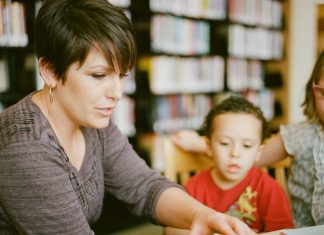 부모와 자녀가 휴교 기간을 알차게 활용하는 방법 Mother reading to children inside of a library. Books in the background holding a book, kids looking and listening intently. https://www.instagram.com/AwCreativeUT/https://www.awedcreative.com/https://www.awcreativeut.com#AwCreativeUT #awcreative #AdamWinger Adam Robert Winger